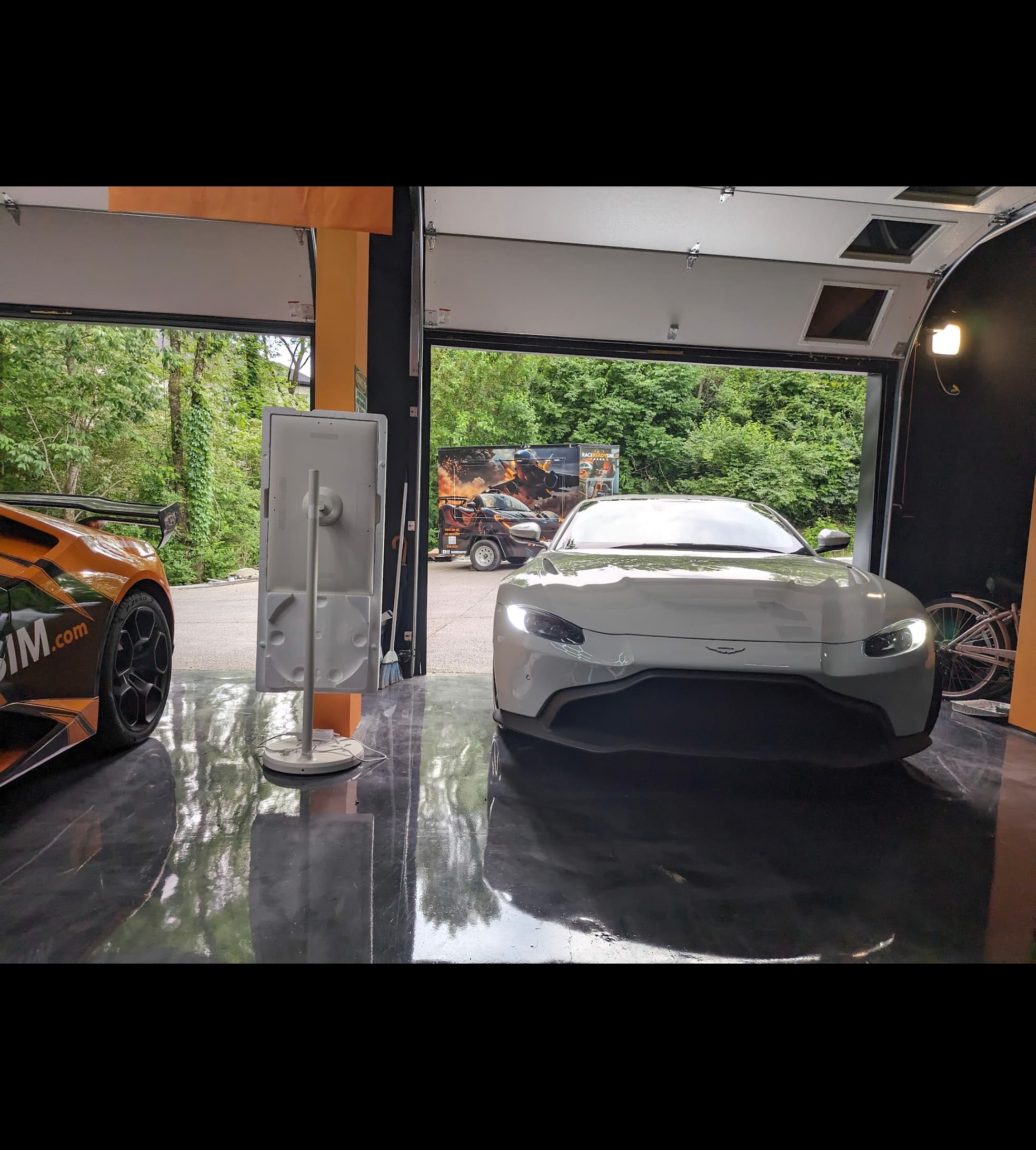 White Aston Martin Vantage parked in a modern garage with reflective floors and open doors.