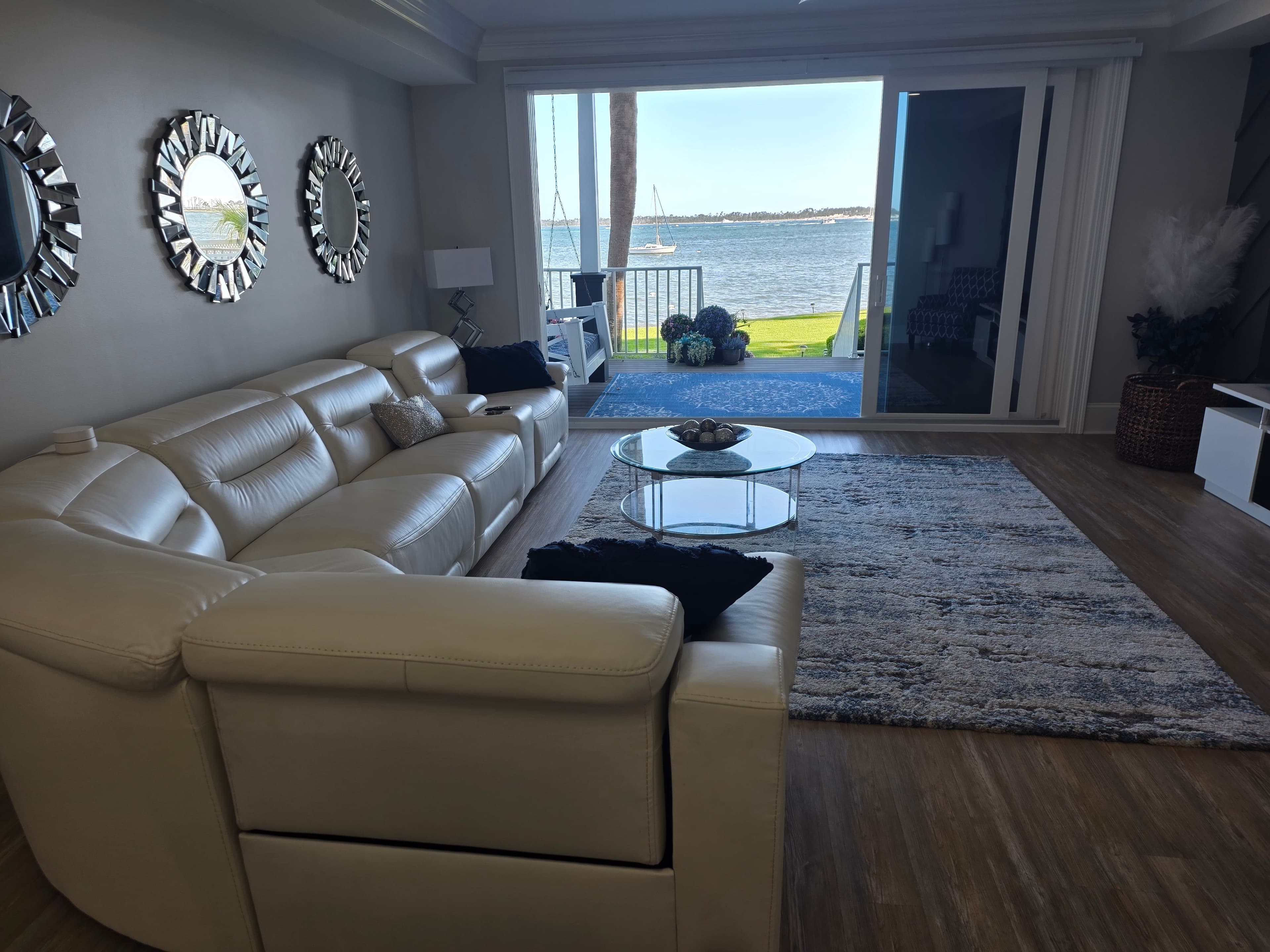 Modern living room with white leather sectional sofa and sliding doors overlooking a scenic bay.